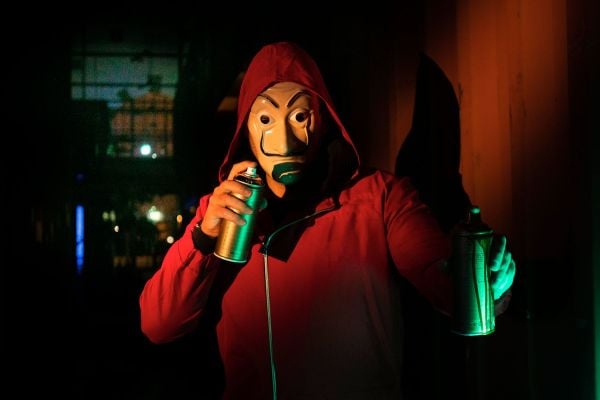 A masked person in a red hoodie holds spray p